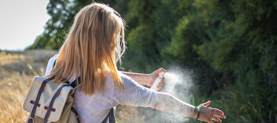Girl spraying arm with bug spray outside