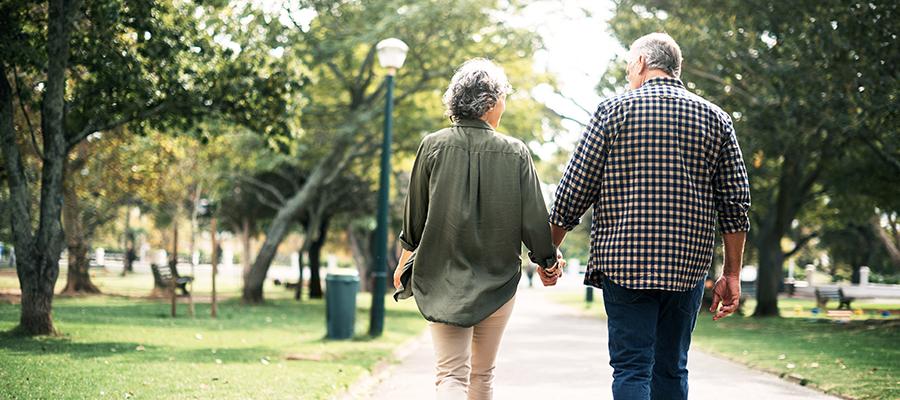 Older couple holding hands walking through park