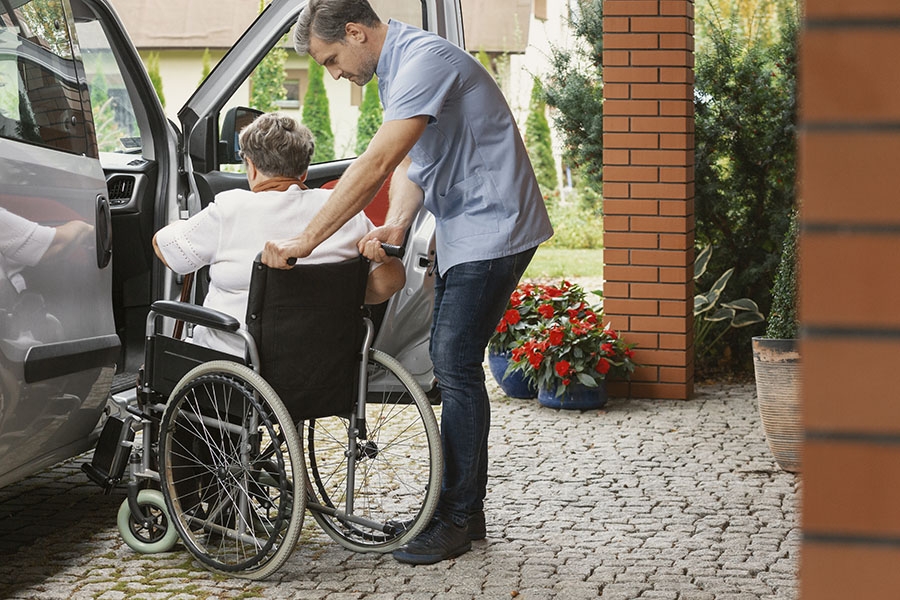 Man helping his mother in a wheelchair into the car.