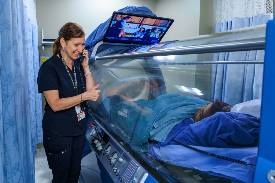 Wound Care Center HBO Tech Stacy Dickel, LPN uses a built-in telephone to communicate with a patient receiving wound care treatment in a hyperbaric chamber.