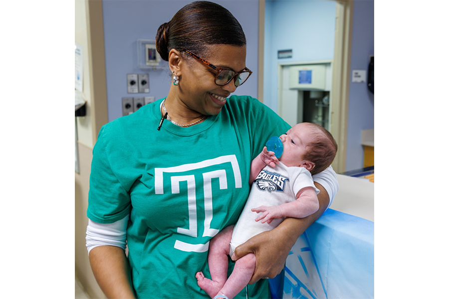 A NICU team member holds one of the babies in their special onesie.