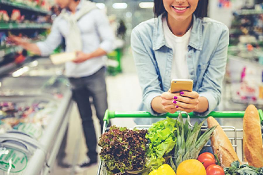 Closeup of woman pushing grocery cart while looking at her phone