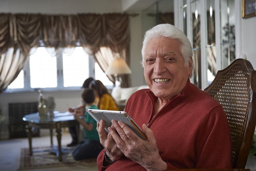 Elderly man holding tablet in living room